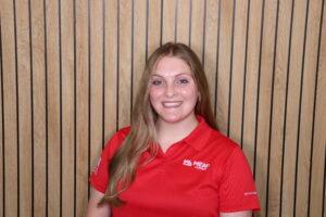 White female headshot wearing a short-sleeved red polo with white embroidered Mead Lumber logo, with long dark blonde hair draped to one side.