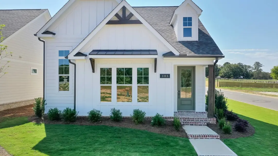 White house with gray roof, brick stoop, sage green and glass door, grass and bushes in the front.