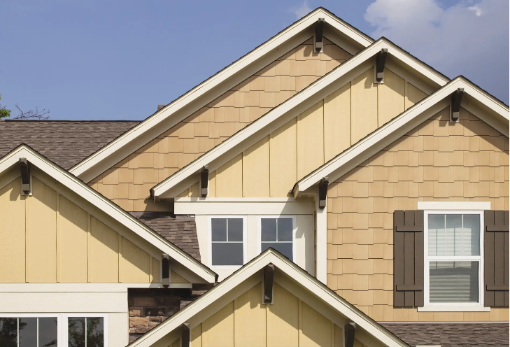 House with 5 gable peaks and vertical cream siding and beige shake siding with wood shutters and windows.