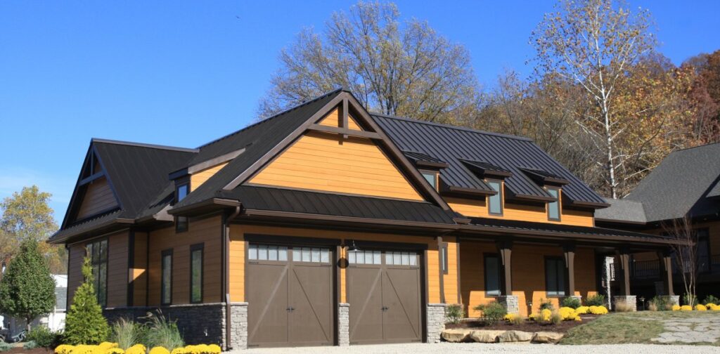 Ranch house with brown 2 car garage doors under a gable peak, dark metal roof by Metal Sales, front porch and caramel colored exterior.