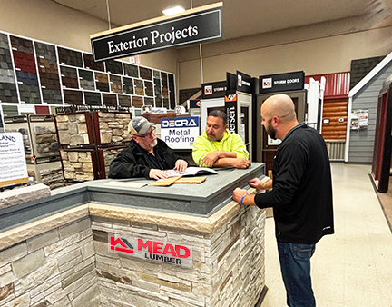 3 male Mead Lumber employees standing at a counter made of stone veneer, looking at paperwork